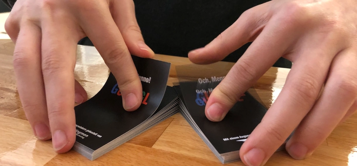 Hände mischen zwei Stapel schwarzer Spielkarten auf einem Holztisch.